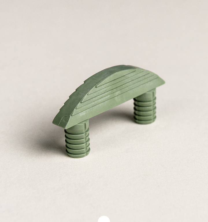 Schräg aufgenommener Möbelverbinder in Grün mit geriffelter Oberseite und zwei konischen Steckdübeln
