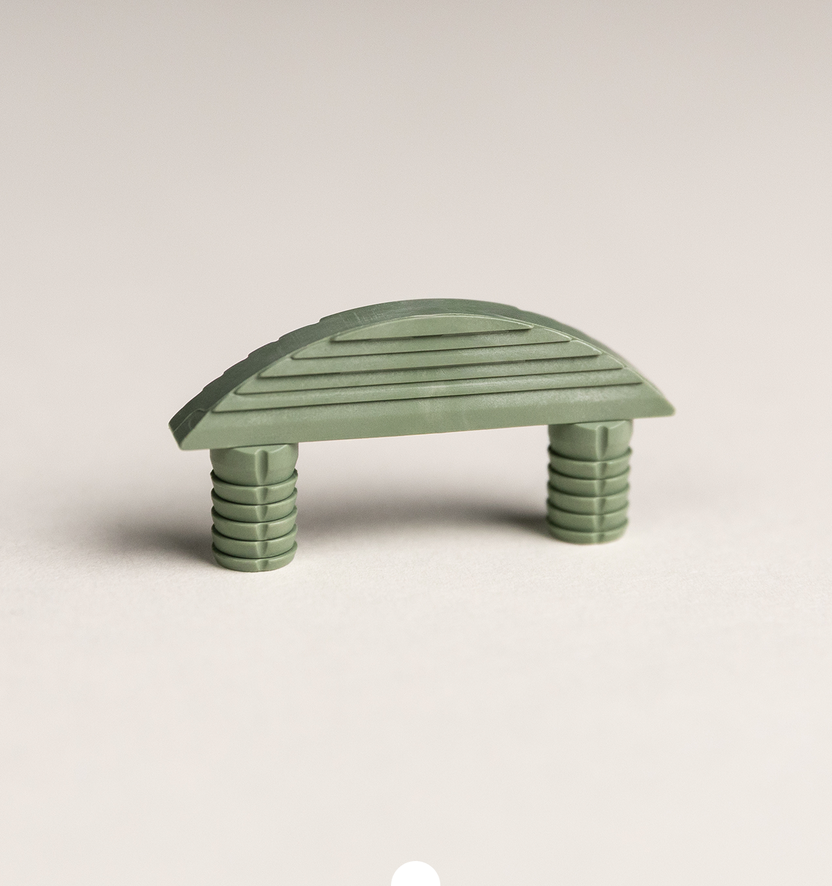 Grüner Möbelverbinder aus Kunststoff mit geriffelter Oberfläche und zwei integrierten Steckdübeln auf hellem Hintergrund
