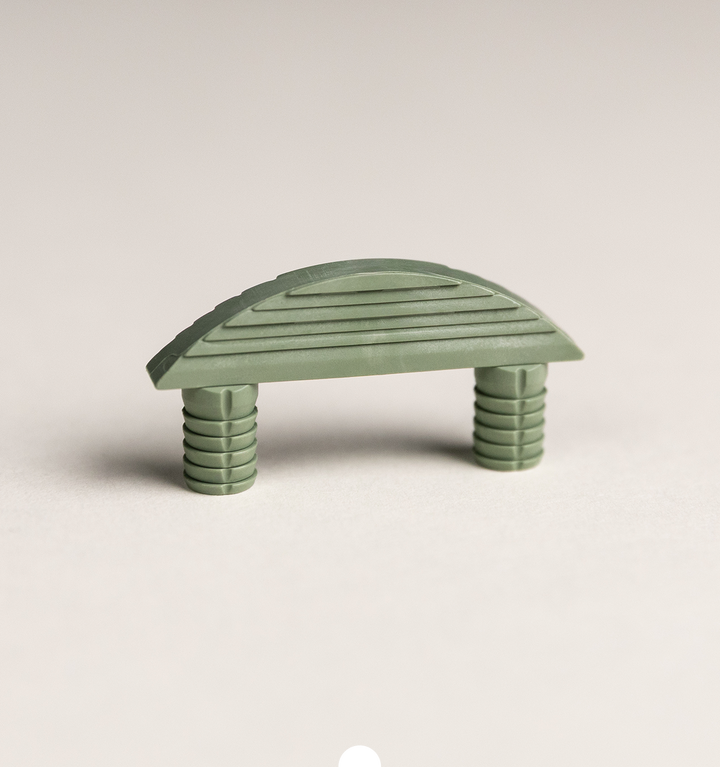 Grüner Möbelverbinder aus Kunststoff mit geriffelter Oberfläche und zwei integrierten Steckdübeln auf hellem Hintergrund
